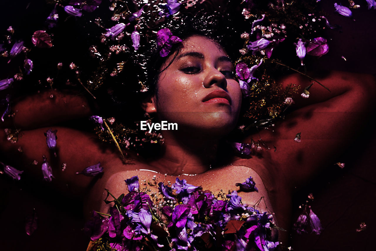 Portrait of shirtless young woman with purple flowers in water