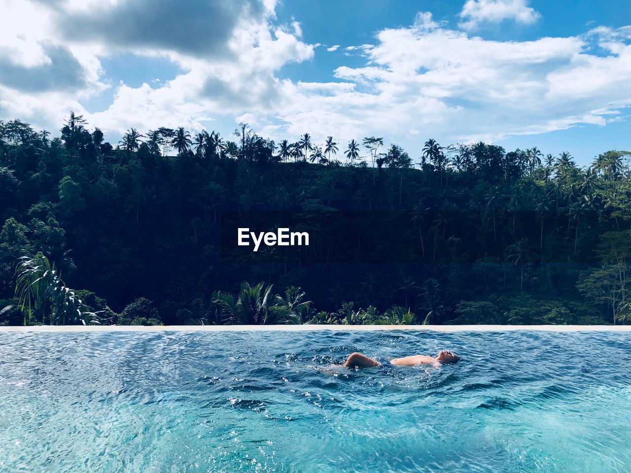 Shirtless man swimming in infinity pool against forest