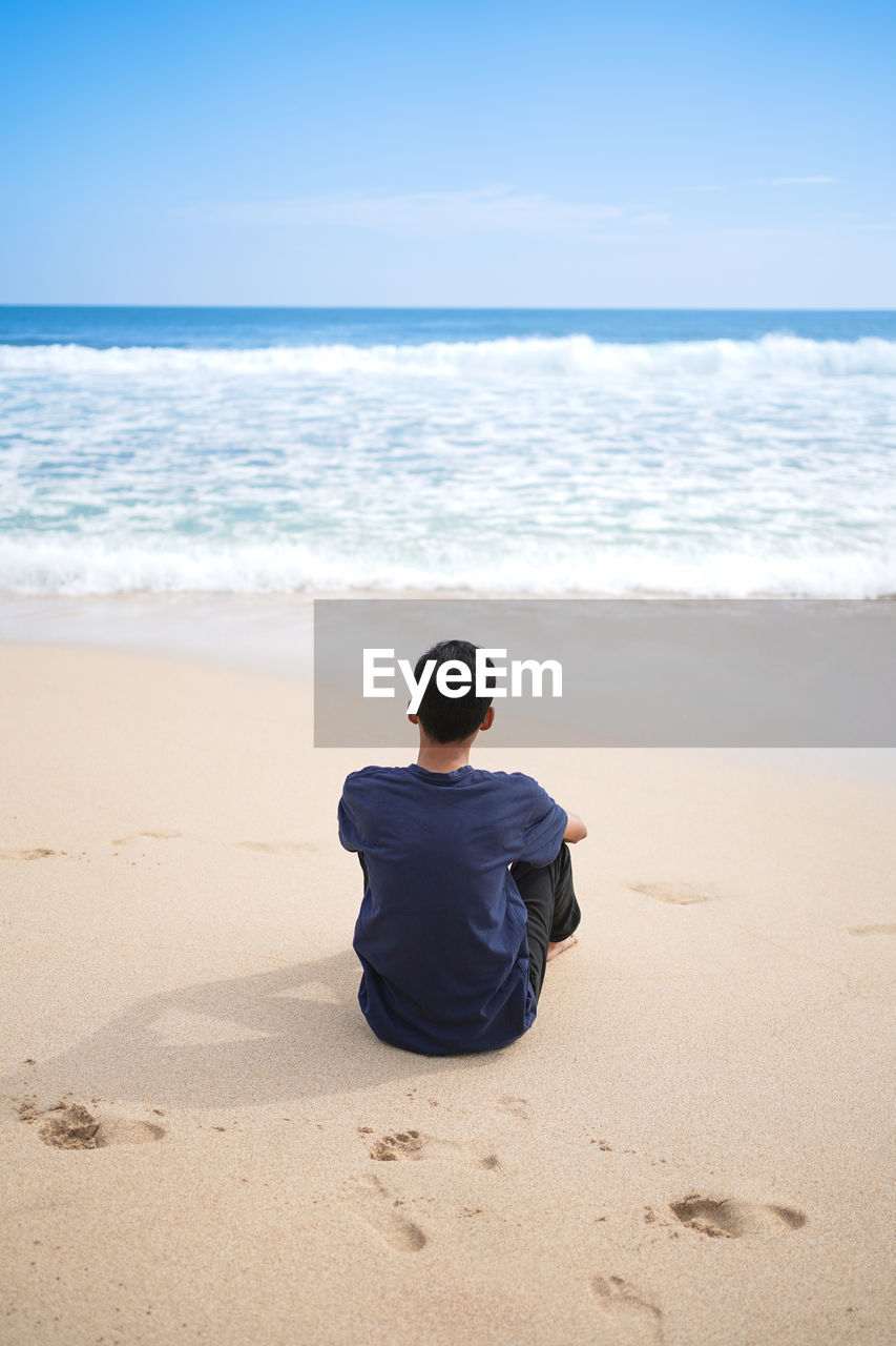 A man in a blue shirt, sitting enjoying the beautiful and clean beach.