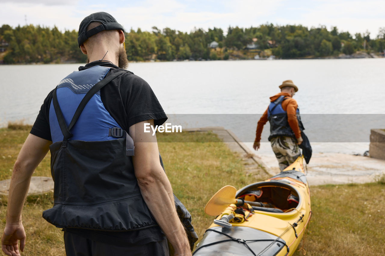 Rear view of men carrying kayak at coast