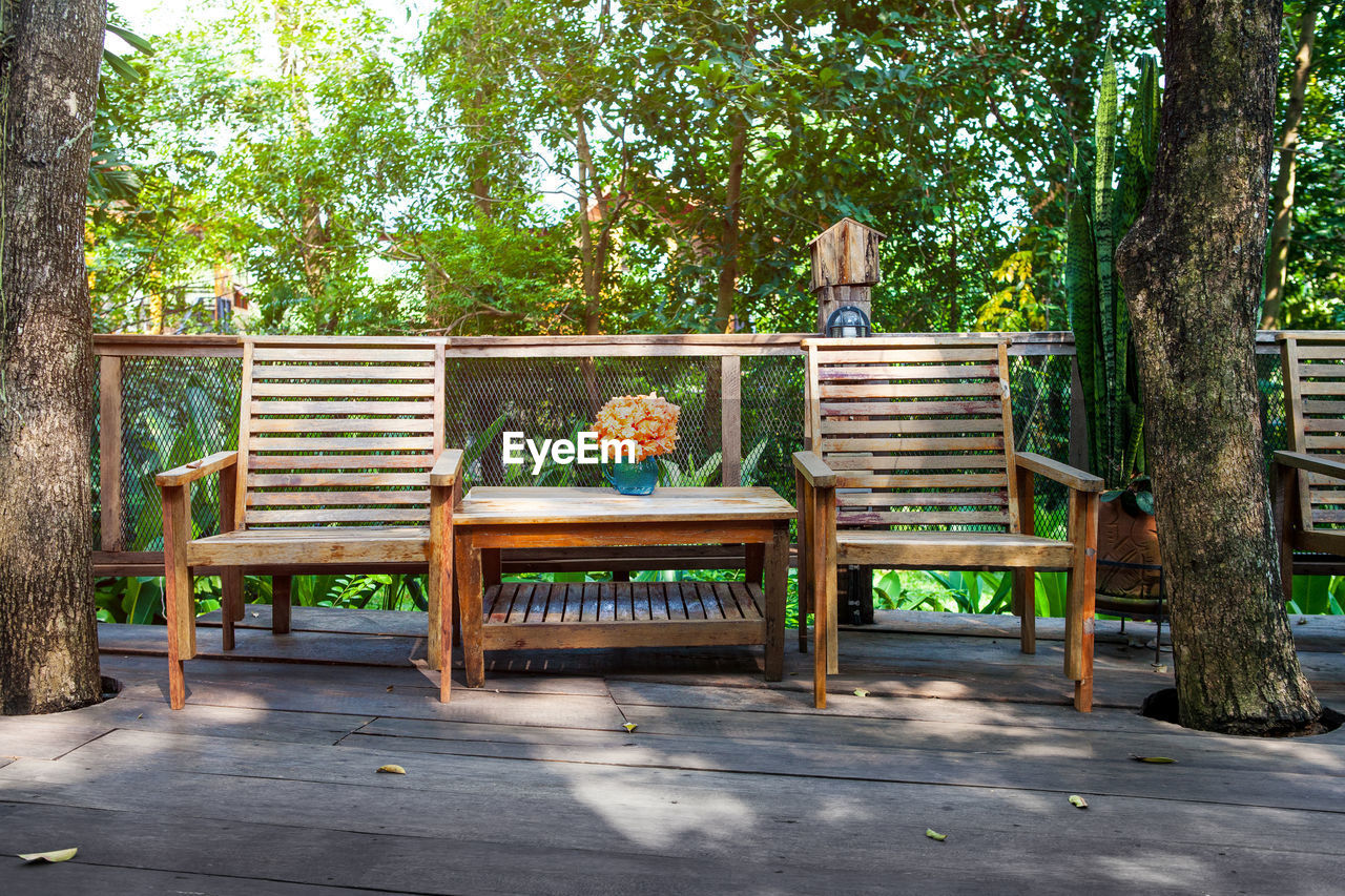 The wooden dining chair is on the balcony in the middle of the big tree