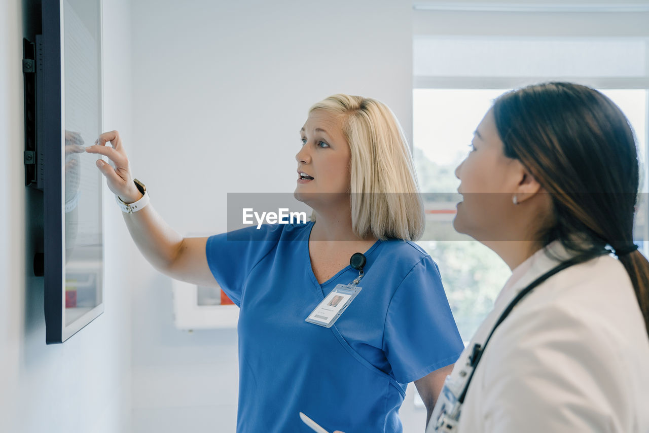 Female doctor pointing at flat screen while discussing with colleague in hospital