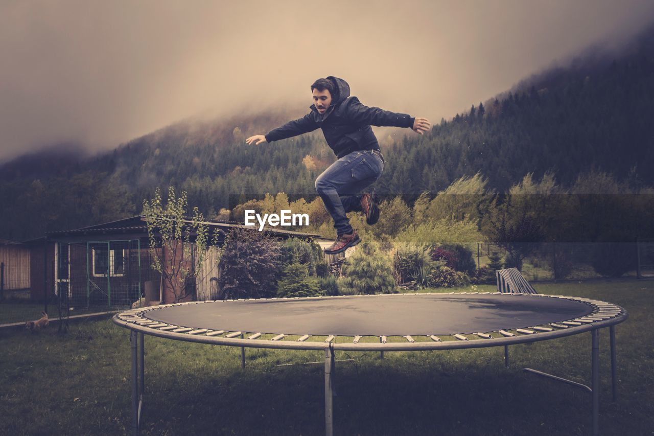 Man jumping over trampoline against sky