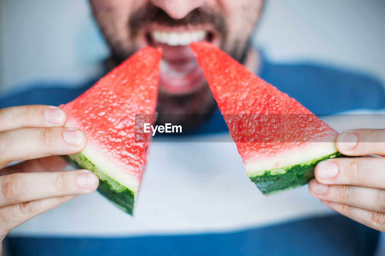 Midsection of man eating watermelons