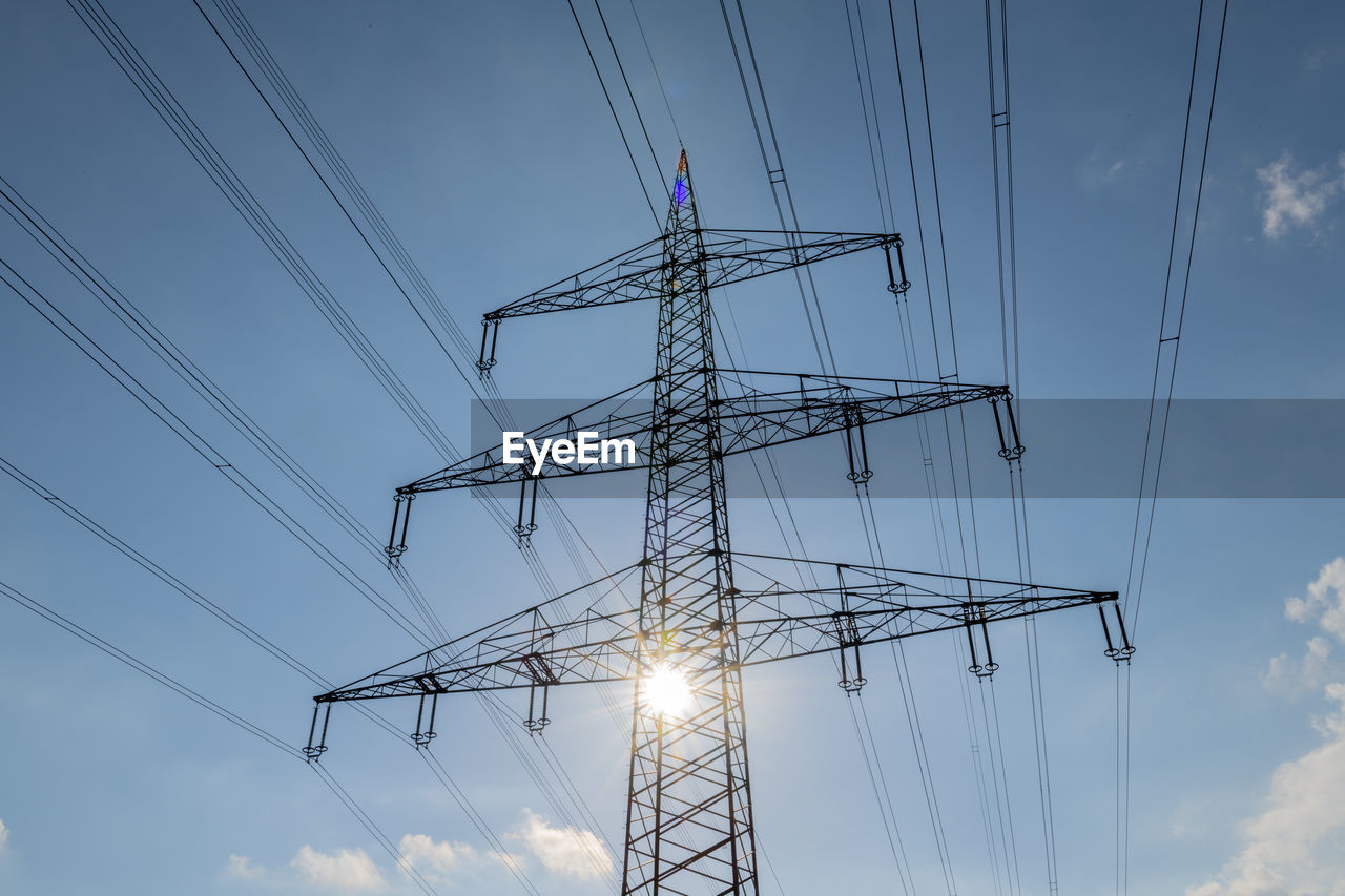 High voltage power line backlit against blue sky