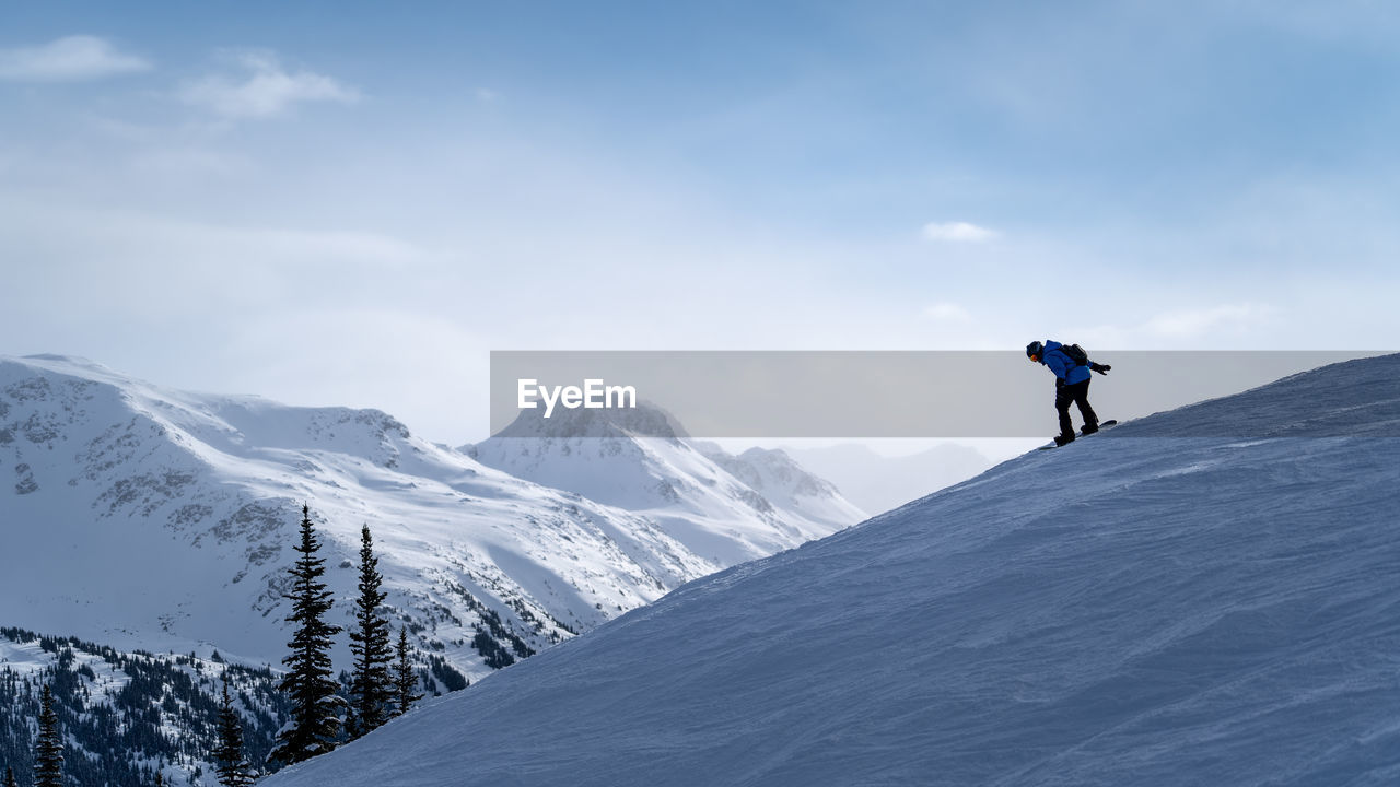 Man snowboarding on snowcapped mountain against sky