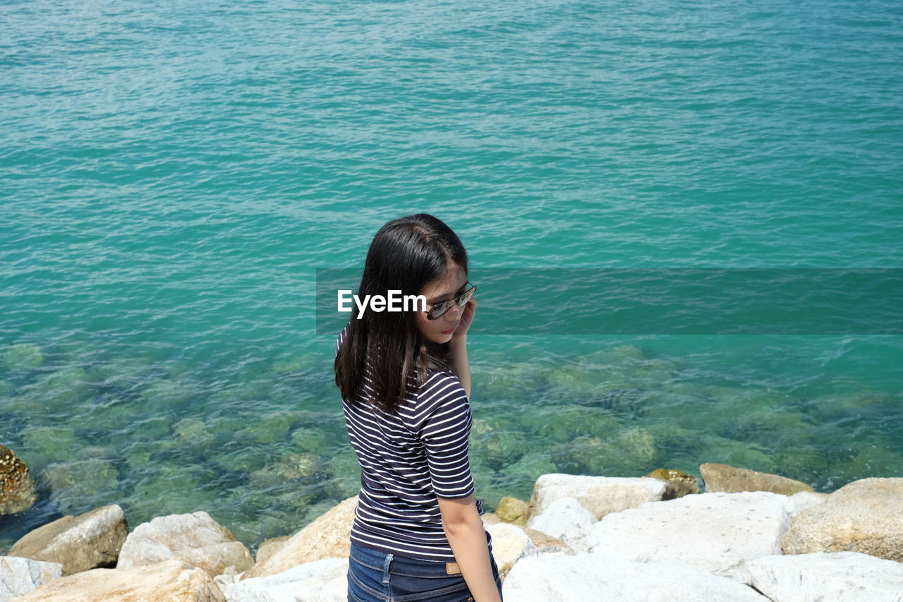 rear view of woman sitting on rock by lake