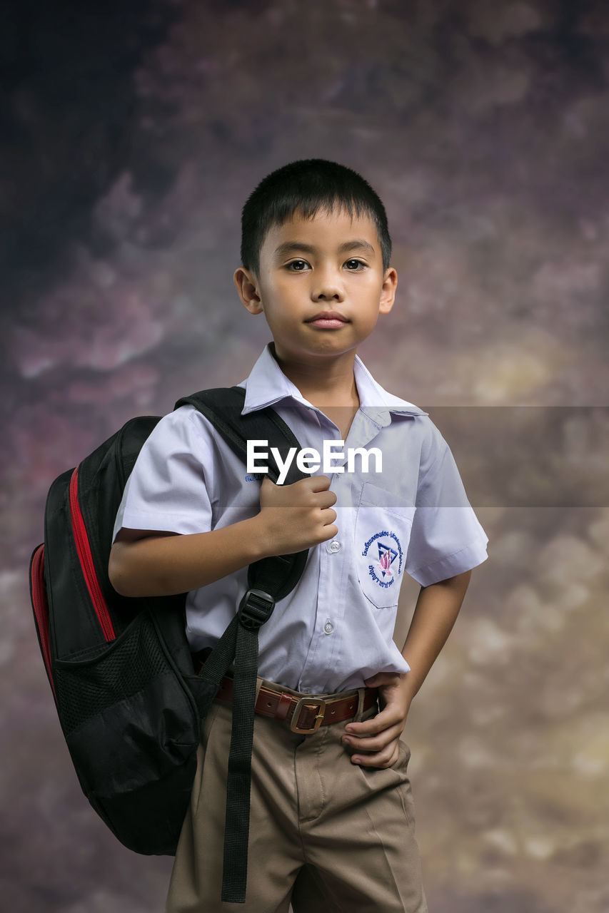 Boy wearing a white shirt school uniform brown pants with a black bag on the first day of school
