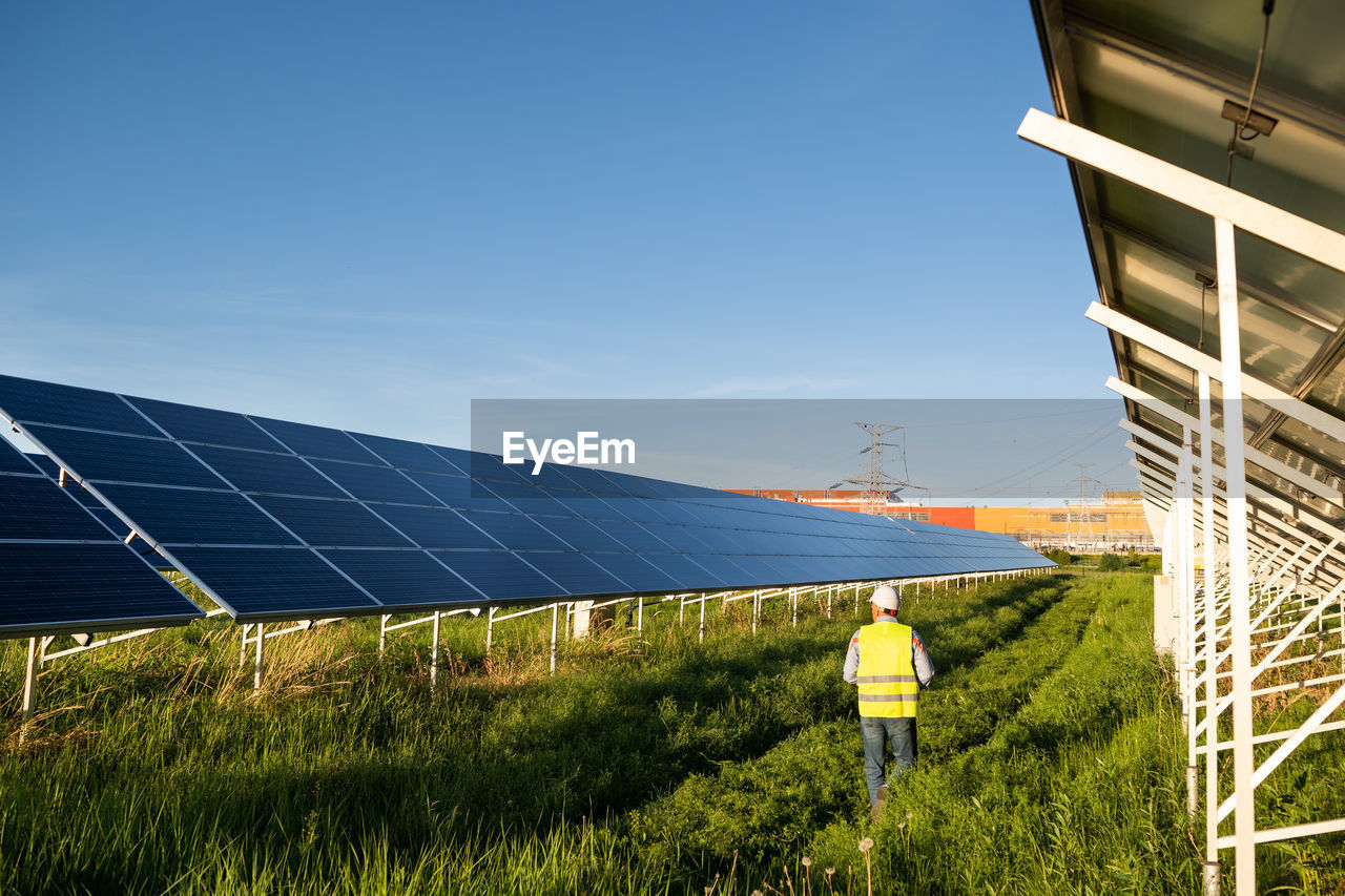 Rear view of engineer walking amidst solar panel