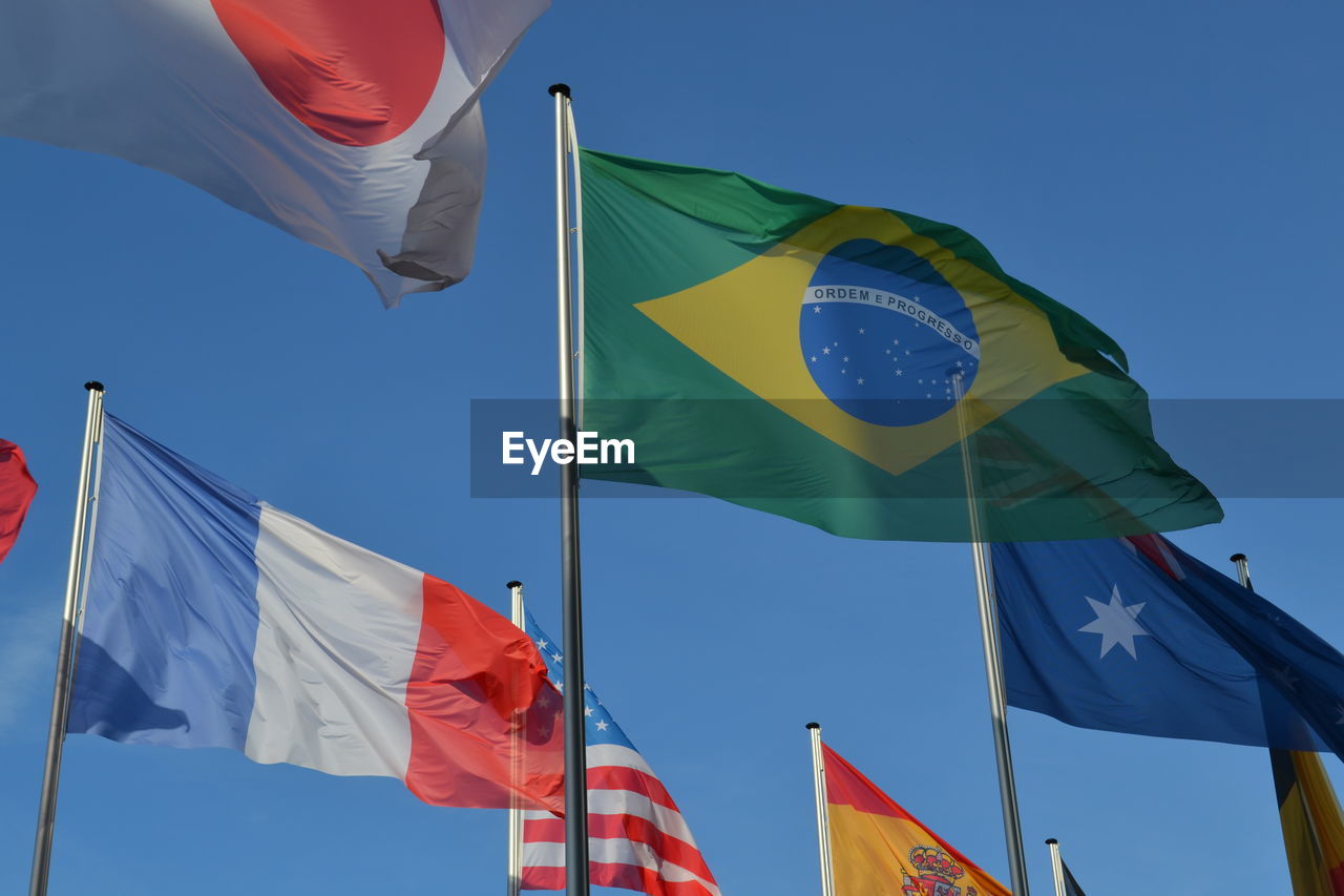 Low angle view of flags waving against clear blue sky