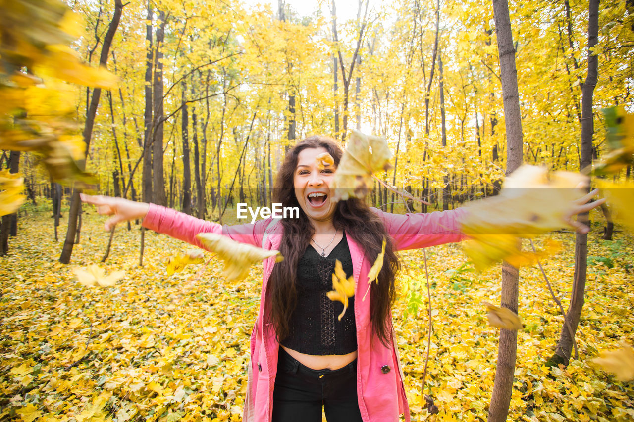 HAPPY YOUNG WOMAN STANDING AGAINST YELLOW TREES