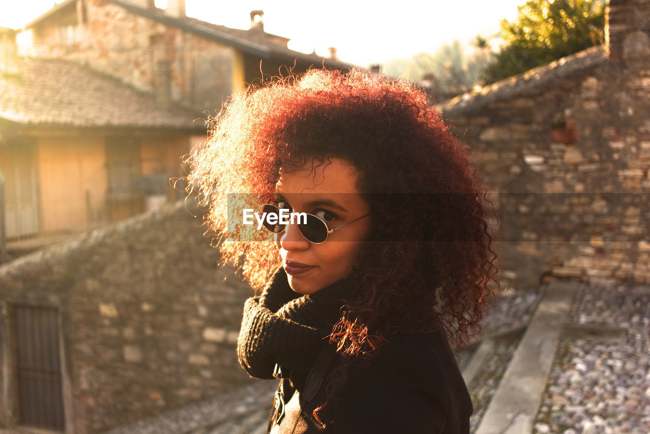 Portrait of woman wearing sunglasses standing against retaining wall