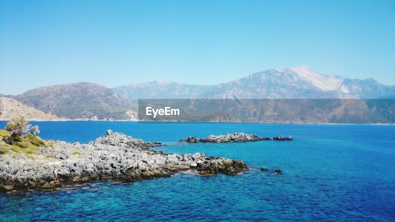 Scenic view of sea by mountains against clear sky