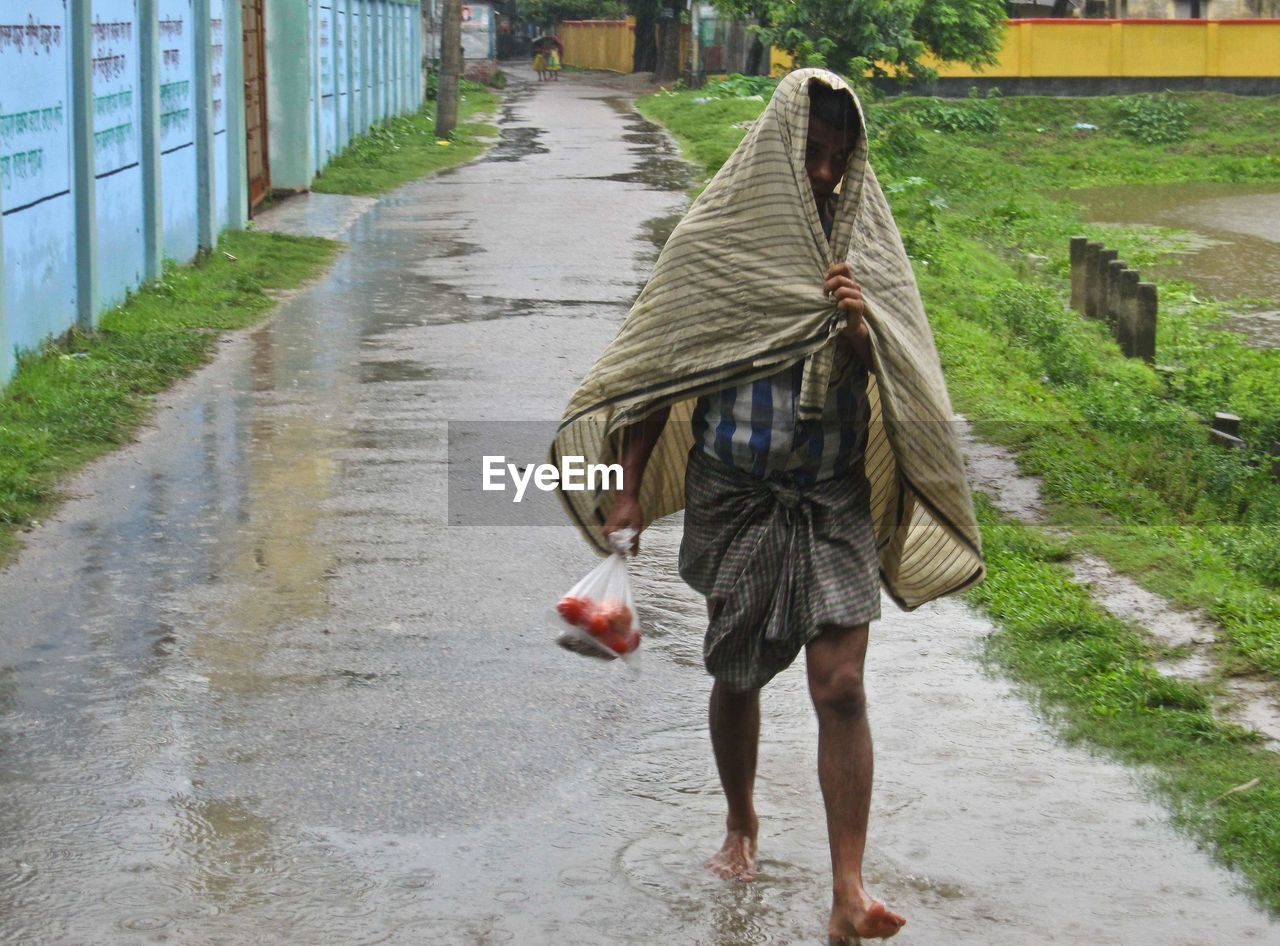 Rear view of woman walking on wet footpath in rainy season