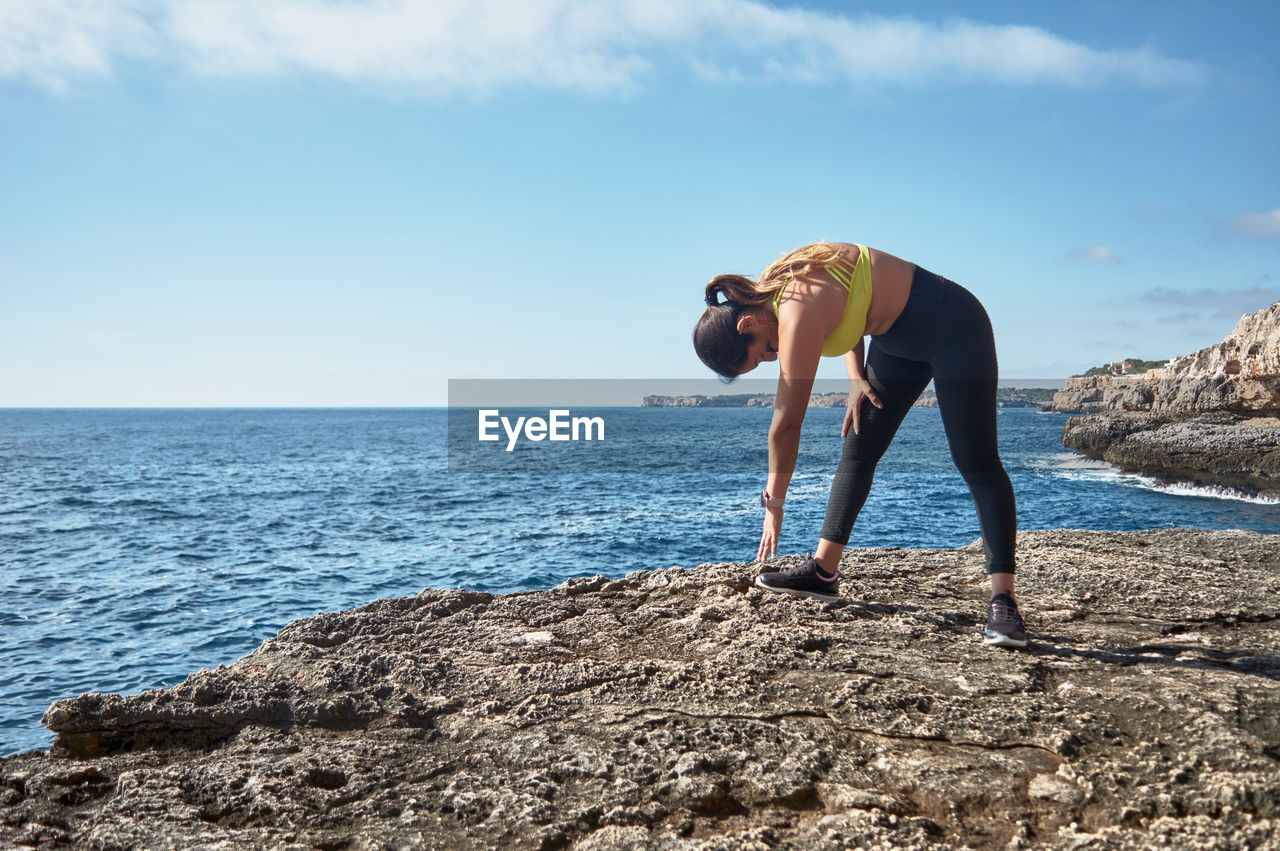 Full length of woman exercising on rock by sea