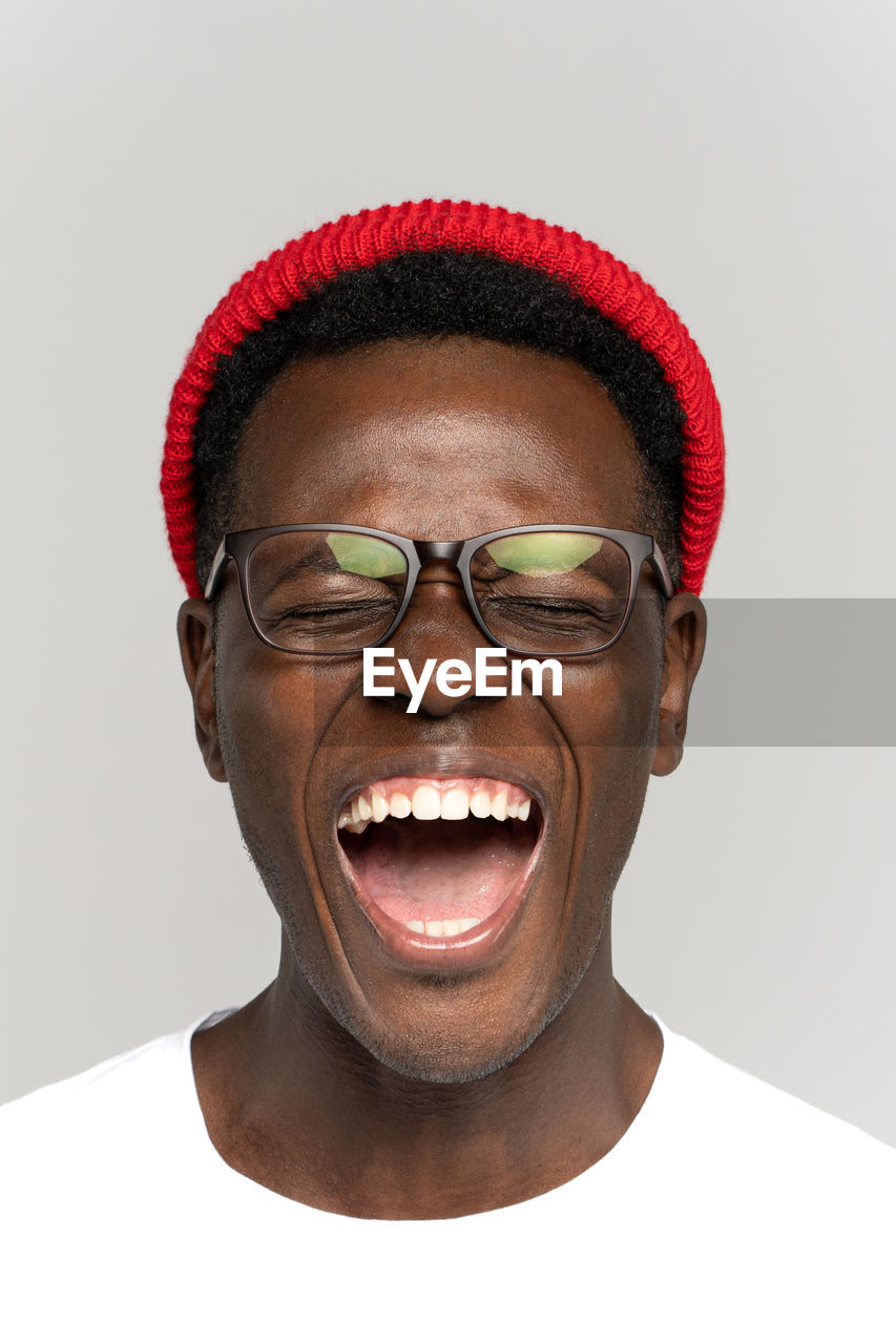 Laughing positive young african hipster man in glasses and red hat in good mood with closed eyes