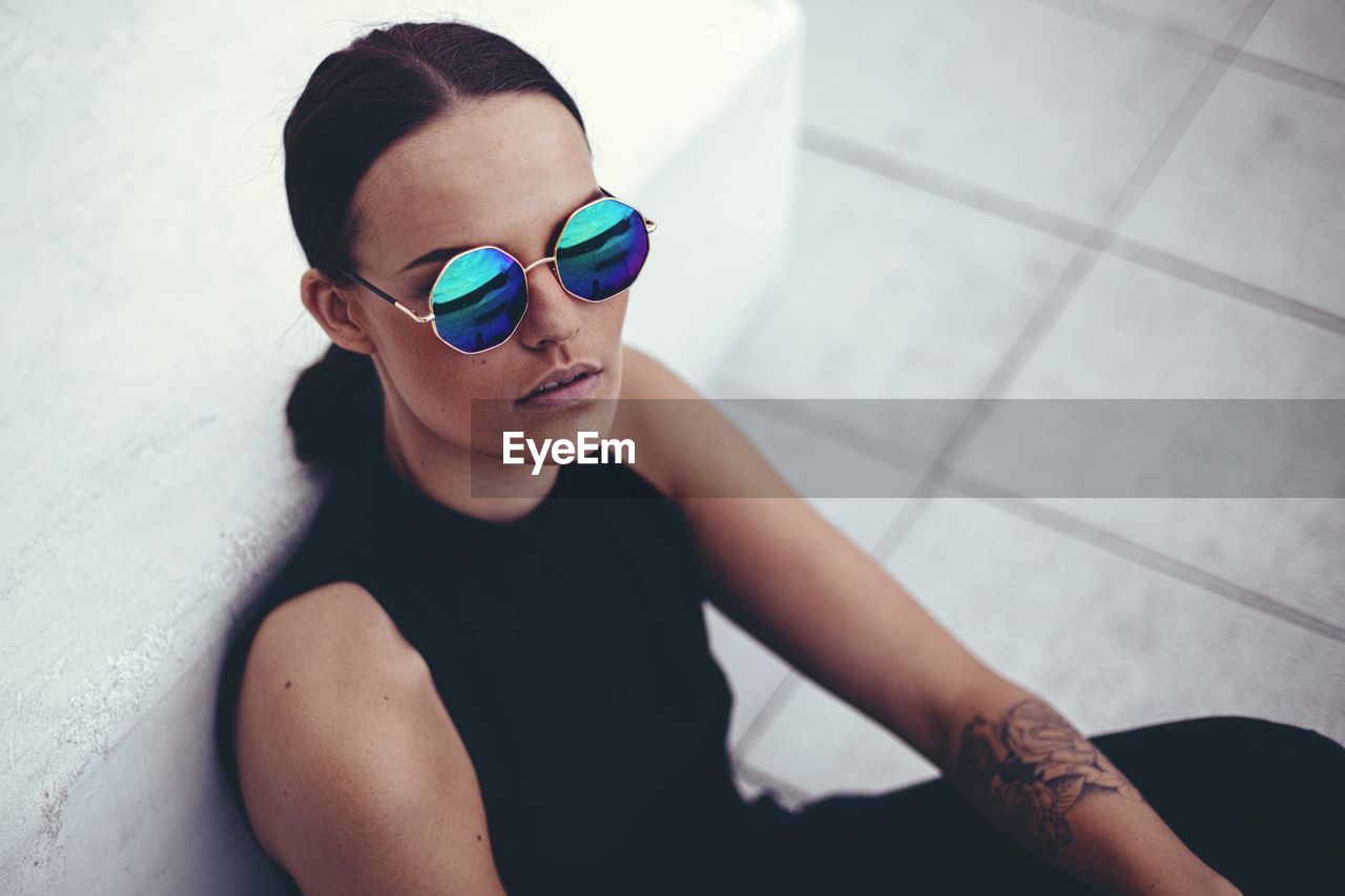 High angle portrait of woman wearing sunglasses by wall