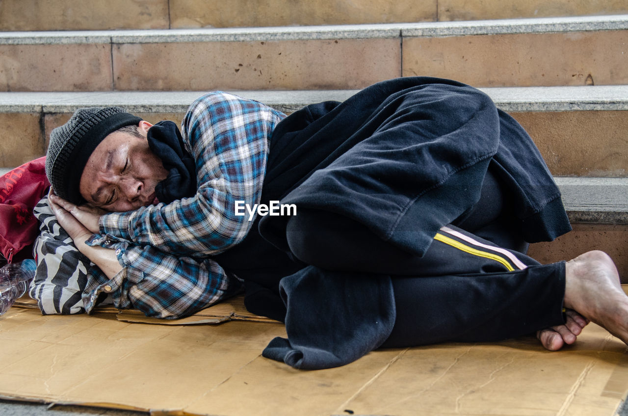 Beggar sleeping against steps in city