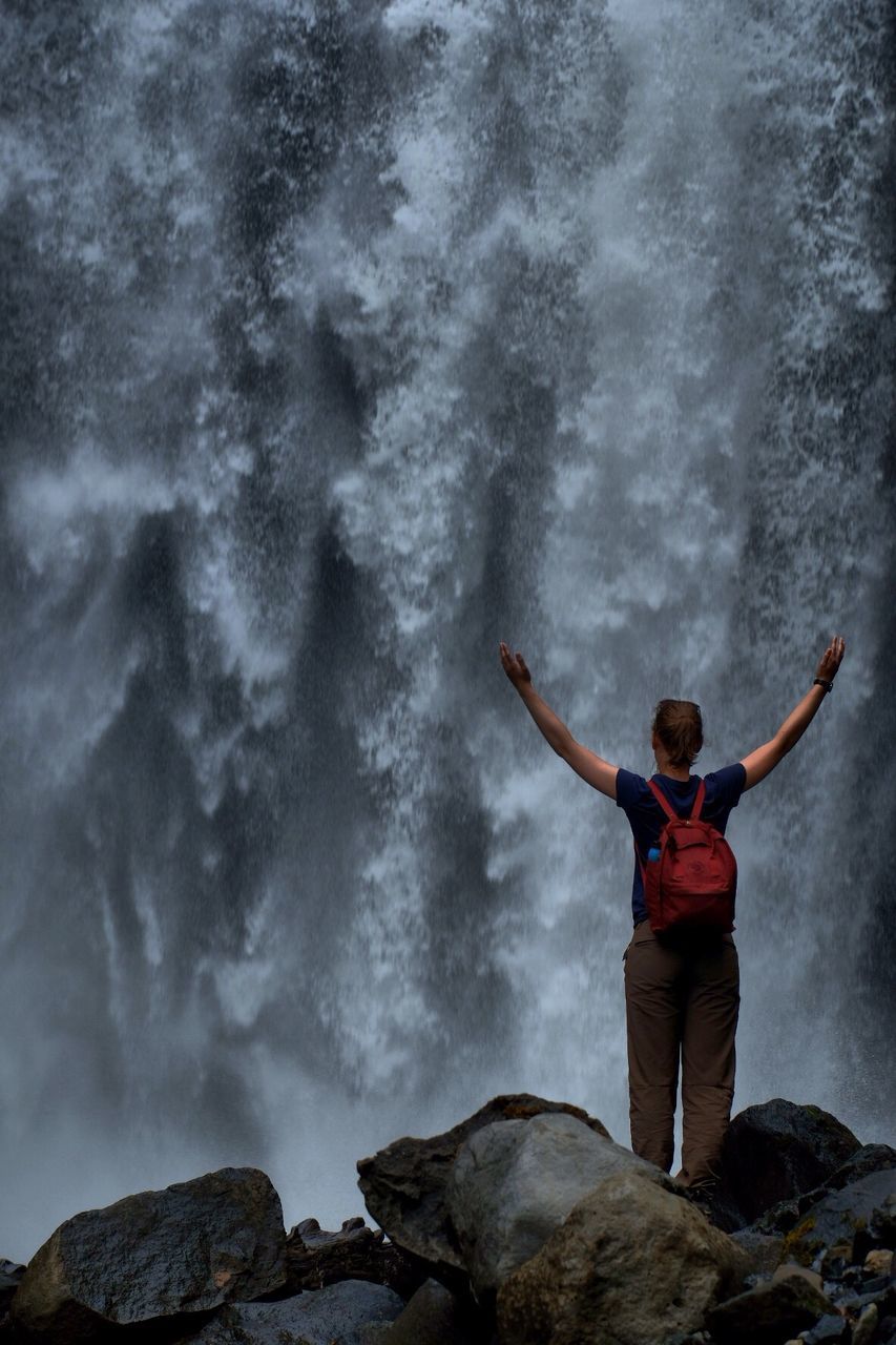 Rear view of man standing on rock against waterfall