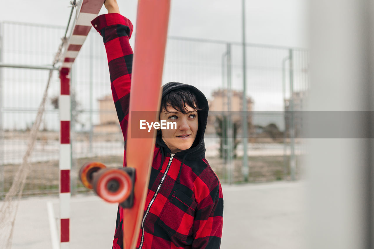 Portrait of young woman wearing hooded shirt leaning on sports goal