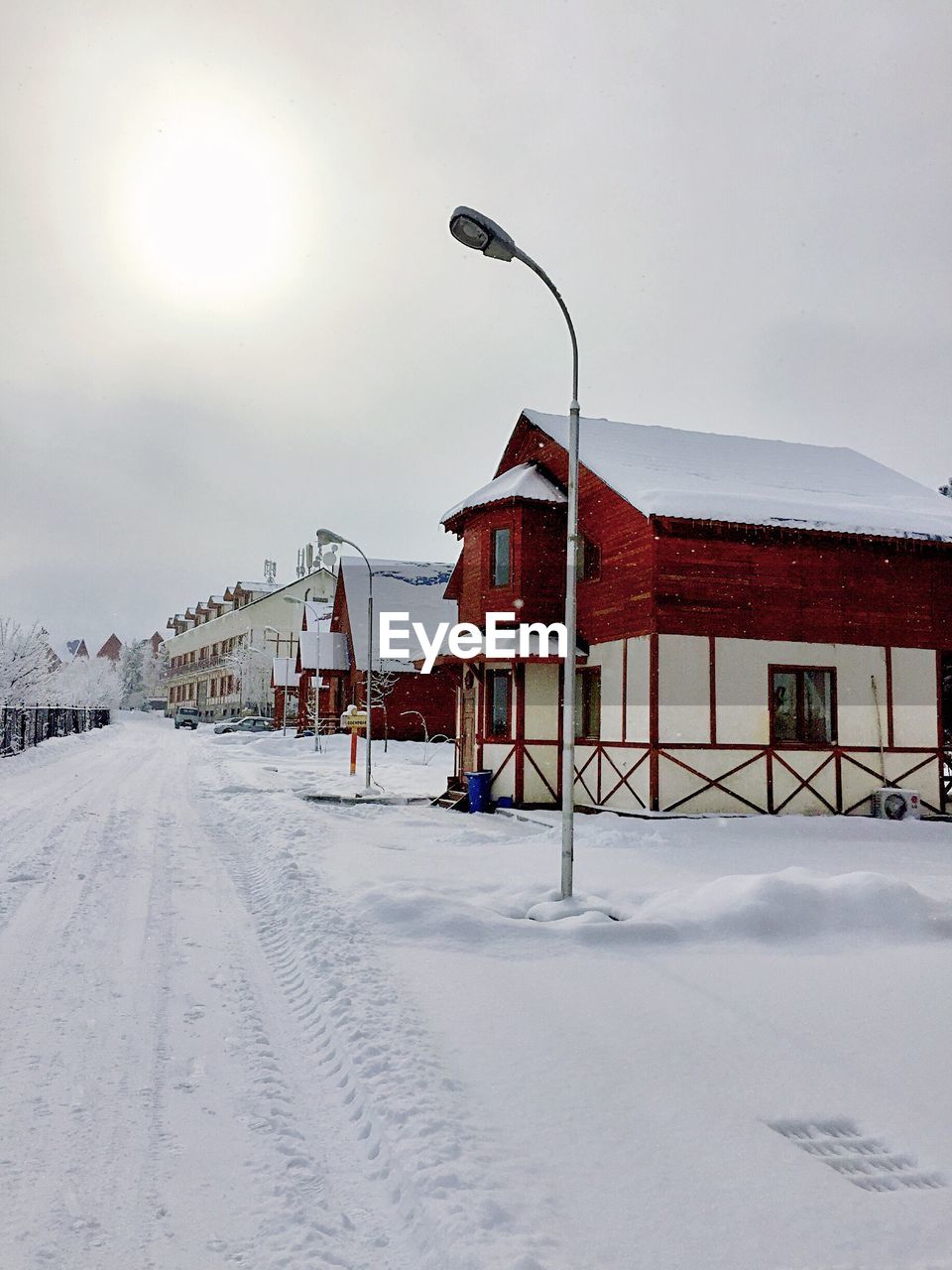 Snow covered road by houses against sky