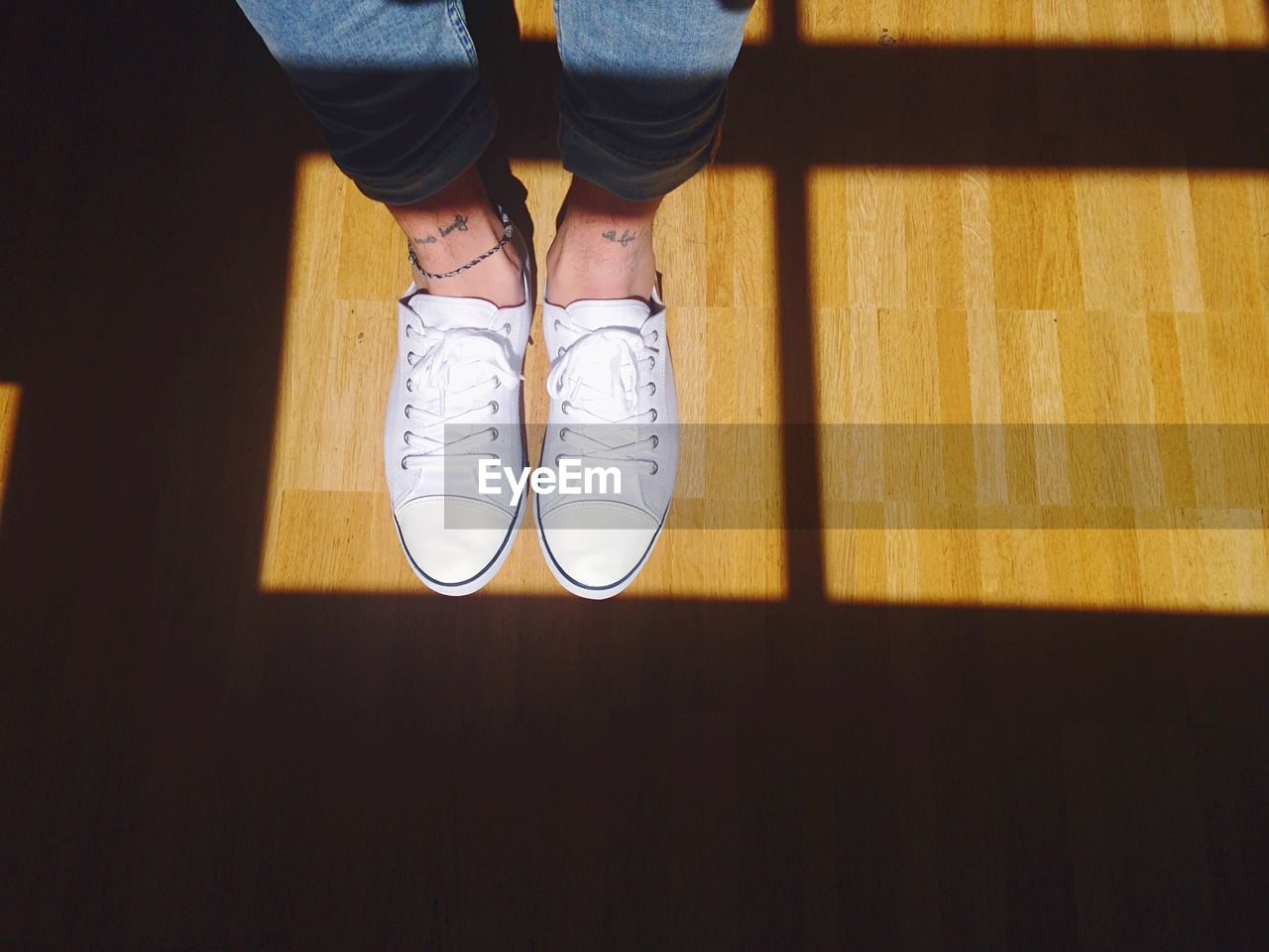 Low section of person wearing white shoes standing on hardwood floor at home
