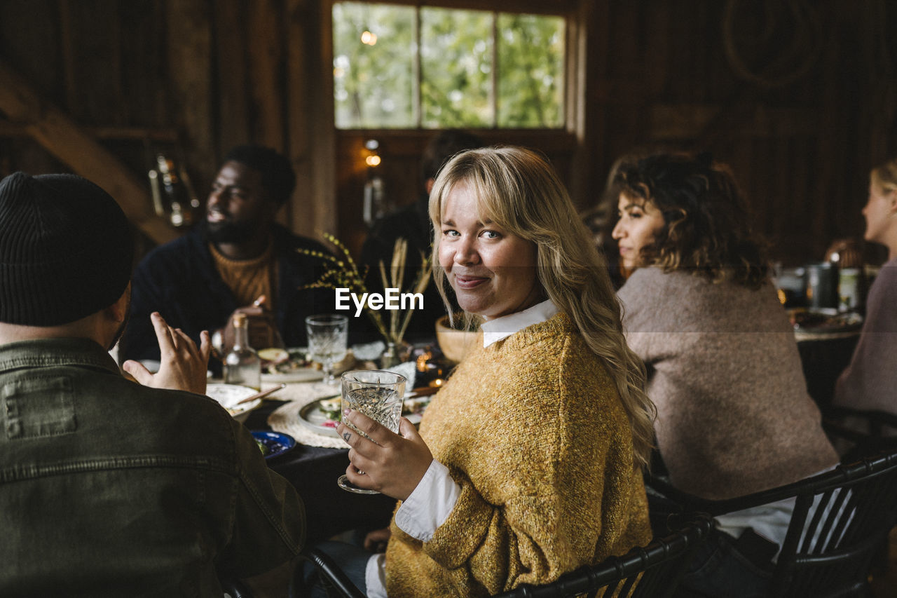 Portrait of smiling woman enjoying with drinking glass by friends during social gathering