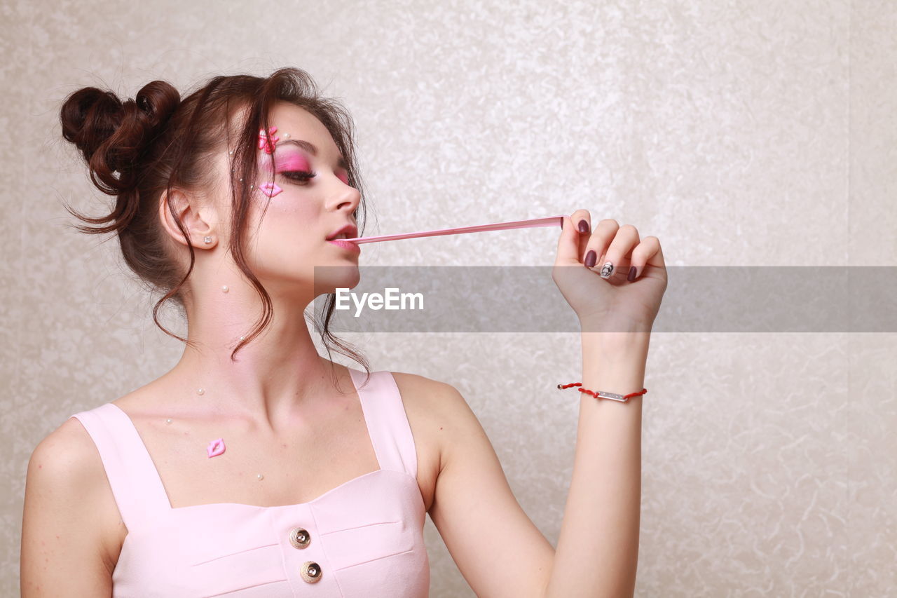 Young woman with pink make-up chewing gum against wall