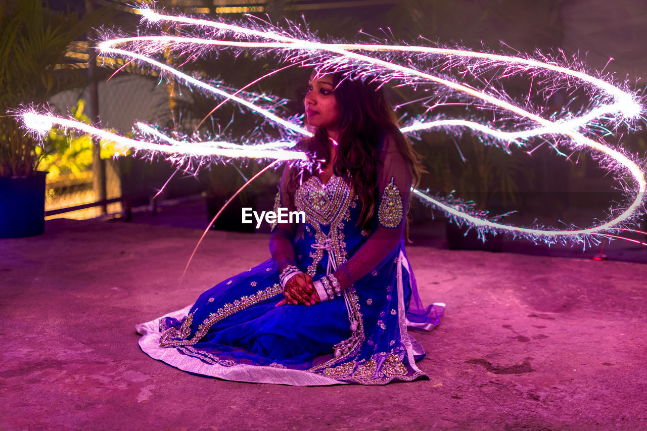 Young woman sitting amidst firework display at night