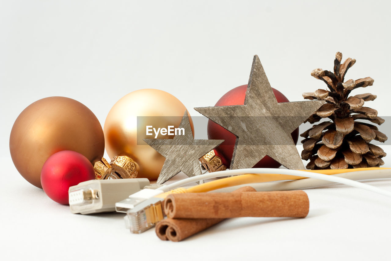 Close-up of christmas decorations and cable against white background 