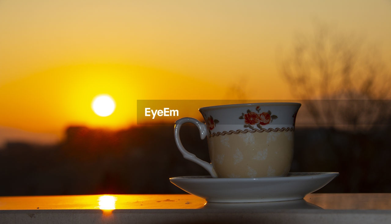 Close-up of coffee cup on table against sky during sunset