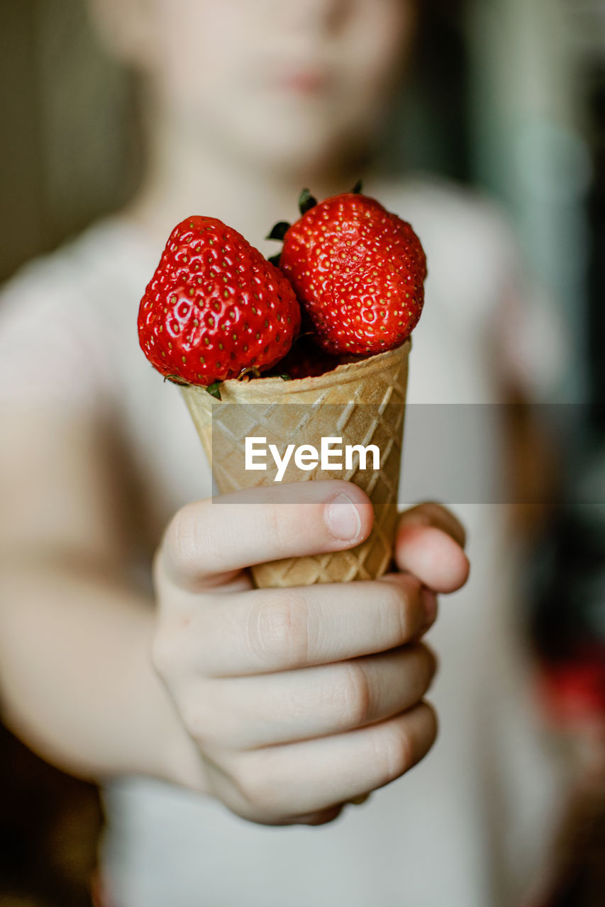 Child hand holding fresh organic strawberries in waffle ice cream cone. red berries in kid hand