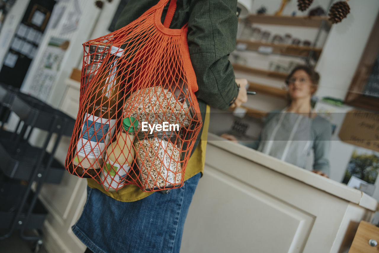 Female customer carrying mesh bag full of groceries in retail store