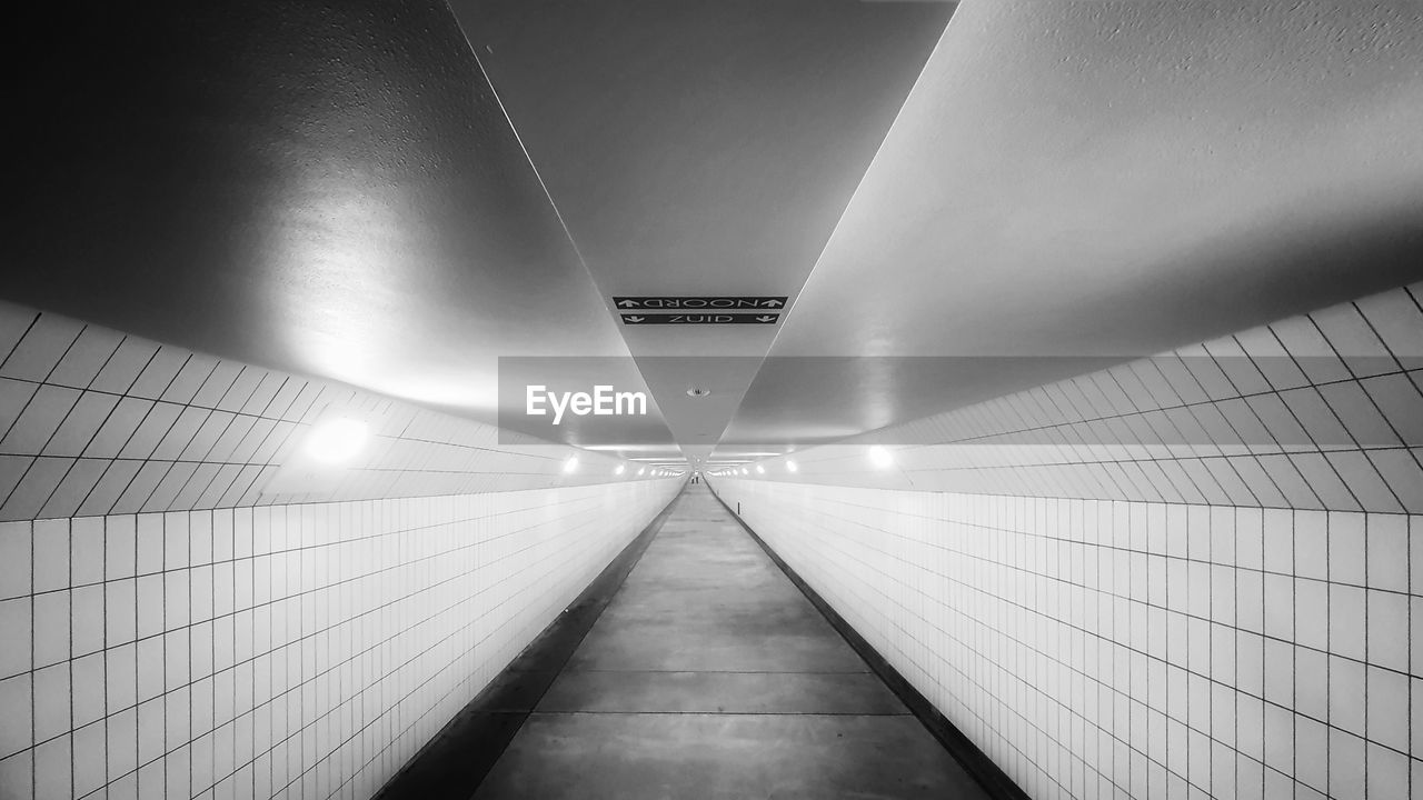 black and white, architecture, light, white, monochrome, illuminated, the way forward, monochrome photography, line, black, indoors, built structure, tunnel, darkness, diminishing perspective, no people, lighting equipment, futuristic, transportation, vanishing point, flooring, subway, ceiling, subway station, tile, wall - building feature, footpath, light - natural phenomenon