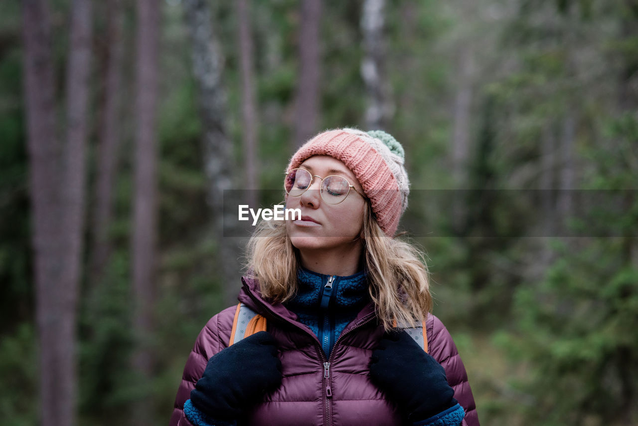 Woman standing in a forest with her eyes closed enjoying being solo