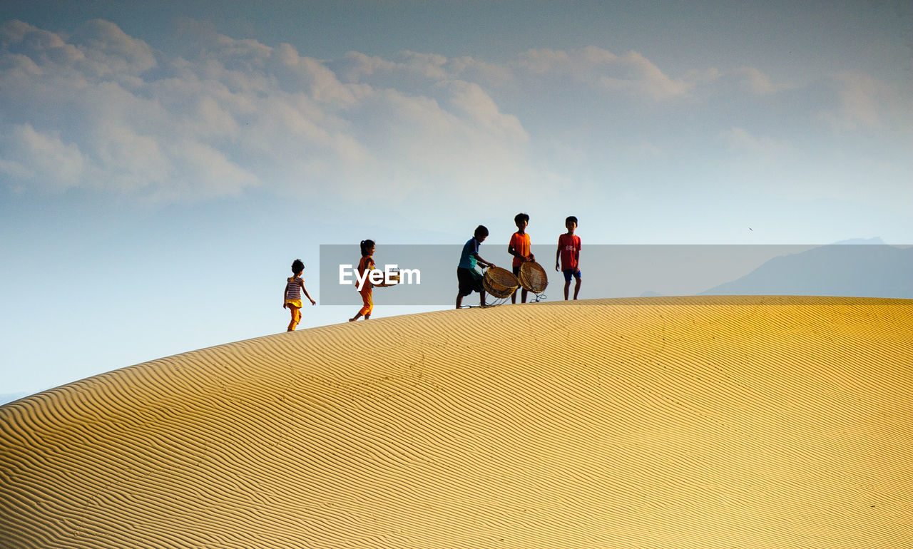 PEOPLE WALKING ON SAND DUNE AGAINST SKY