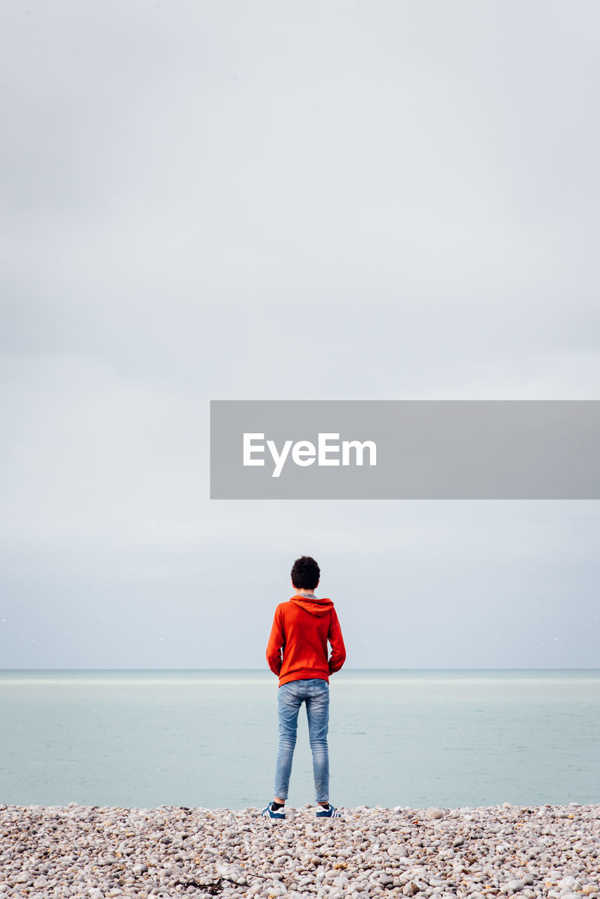 Rear view of boy standing at beach against sky