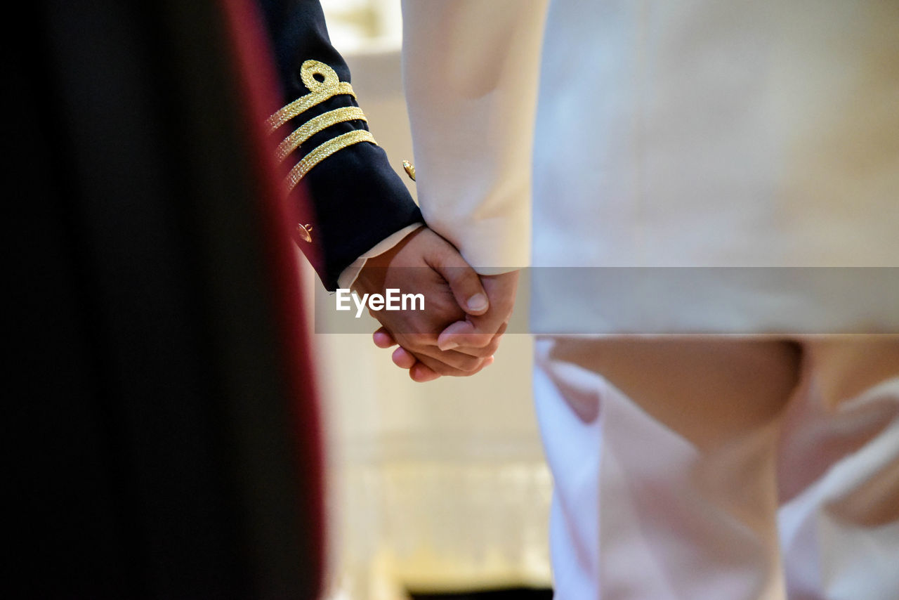 Midsection of men in uniform holding hands