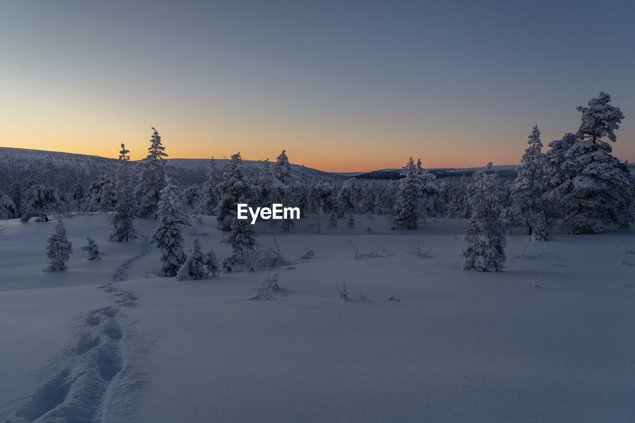 Scenic view of snow covered landscape against clear sky during sunset