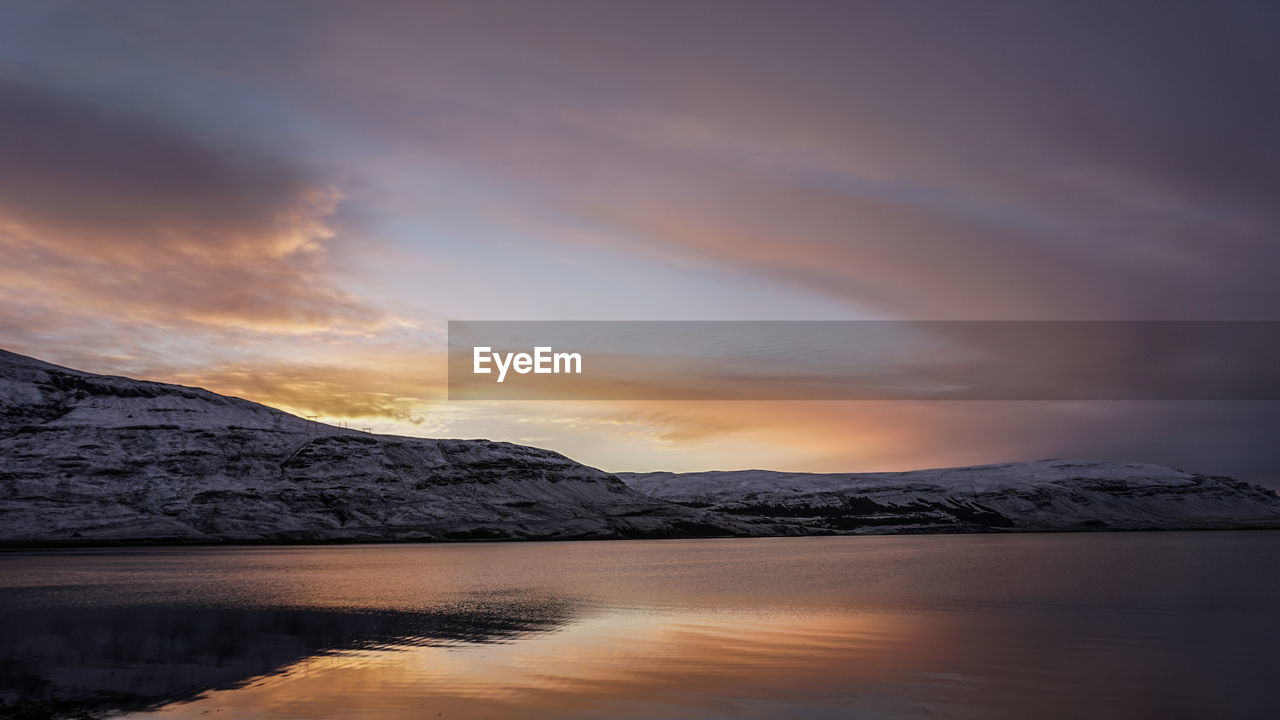 Scenic view of lake by snowcapped mountains against sky during sunset