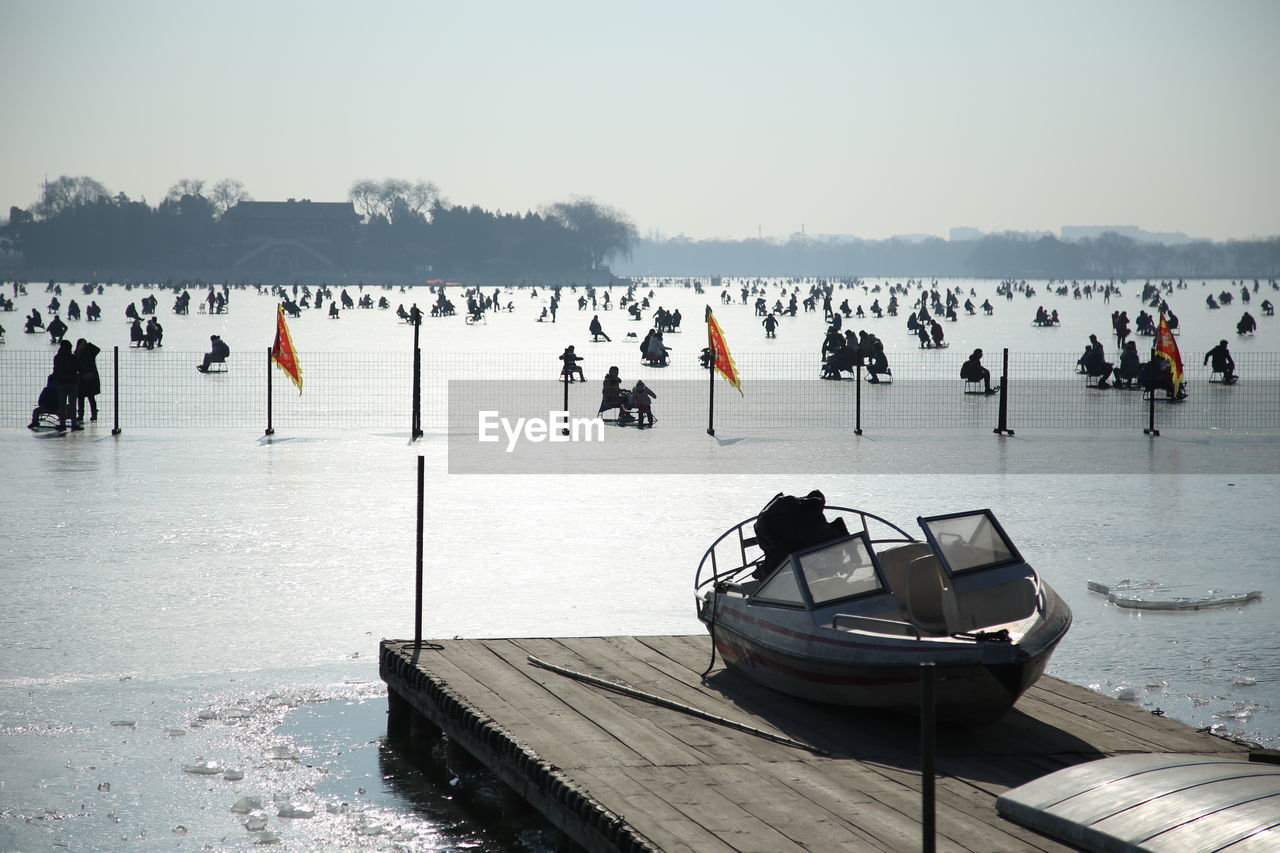 People riding sleds on frozen lake against sky