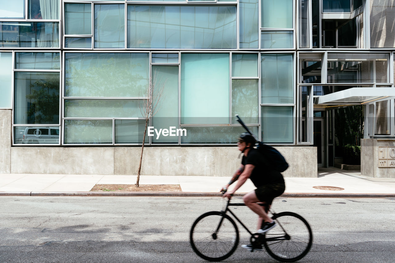 FULL LENGTH OF MAN RIDING BICYCLE ON STREET AGAINST BUILDING