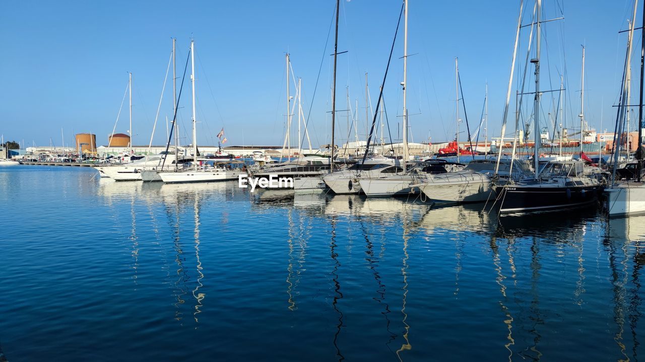 water, nautical vessel, transportation, marina, sailboat, mode of transportation, dock, pole, mast, moored, sea, harbor, sky, nature, no people, boat, reflection, blue, clear sky, vehicle, ship, day, sailing, port, tranquility, yacht, outdoors, beauty in nature, watercraft, travel, bay, waterfront, sunlight, sunny, tranquil scene, travel destinations