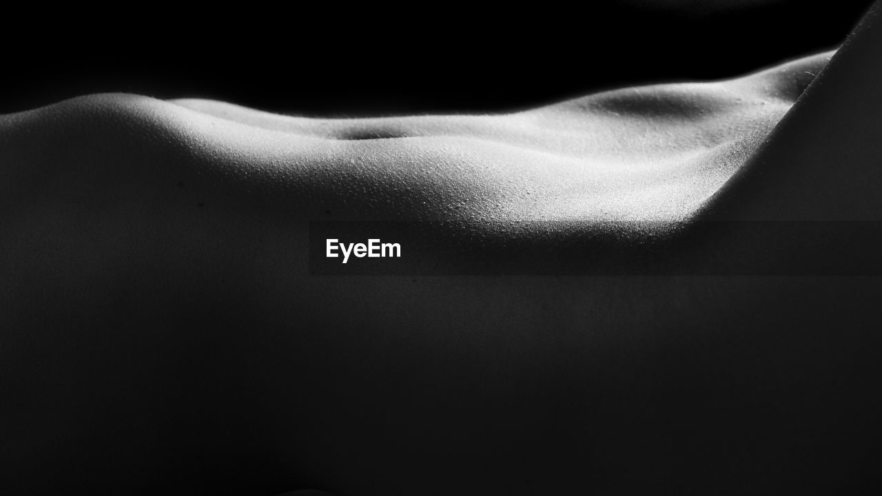 Midsection of naked woman against black background