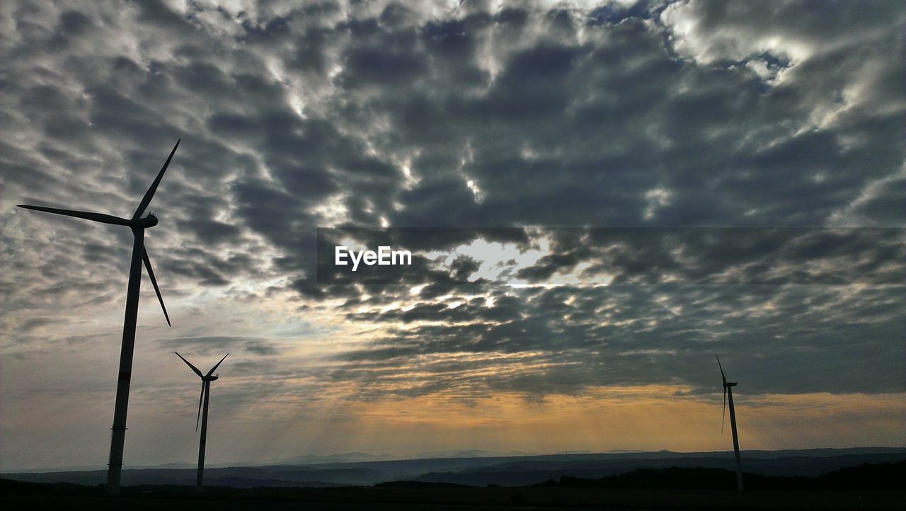 Low angle view of windmills on field against cloudy sky during sunset