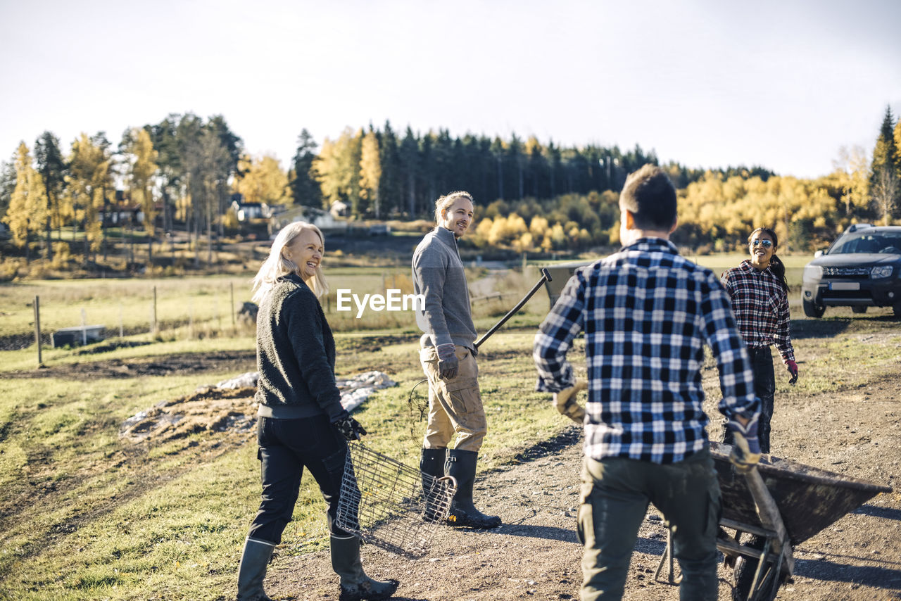 Multi-ethnic male and female farmers with equipment walking on field