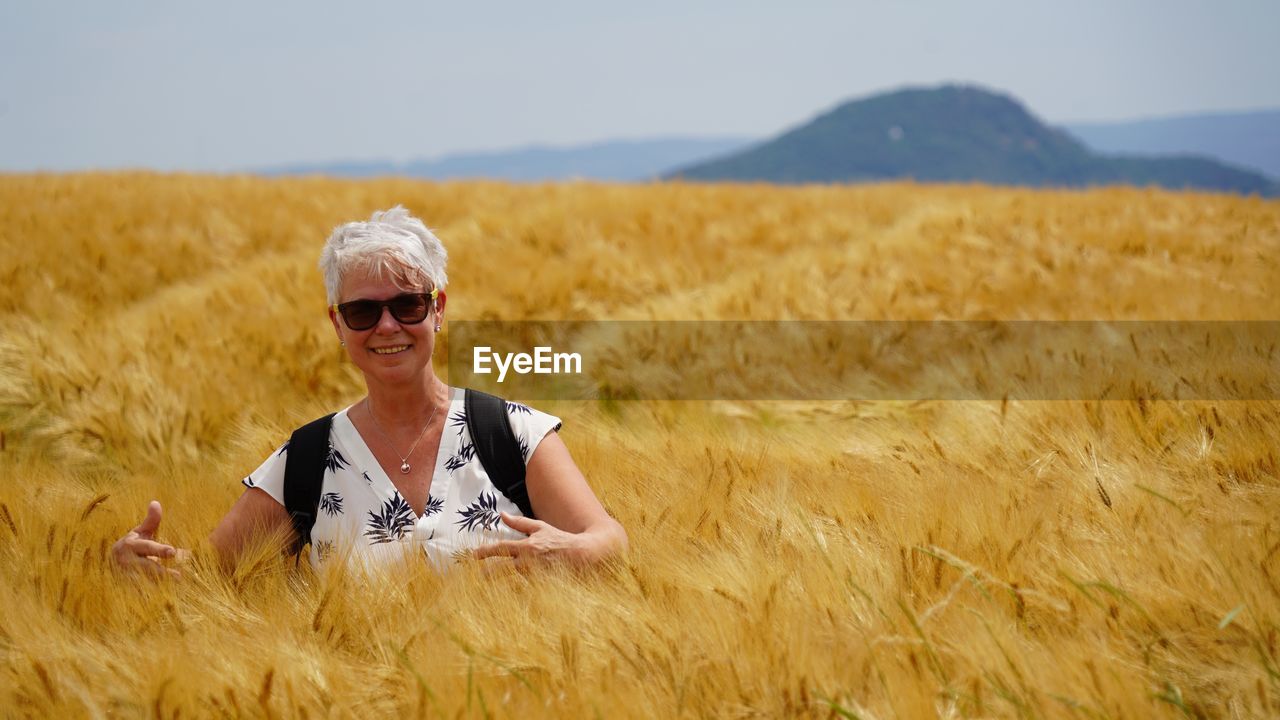 Woman wearing sunglasses on barley field against sky