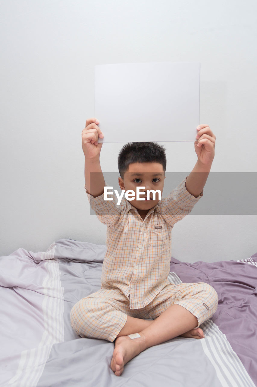 BOY LOOKING AWAY WHILE SITTING ON BED