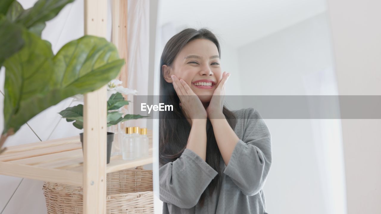 Over a spa background, a young gorgeous woman with a towel on her head cheerfully touches her.