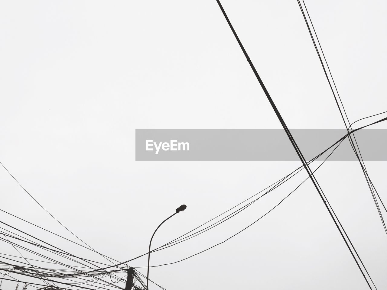 Low angle view of silhouette street light and power lines against clear sky